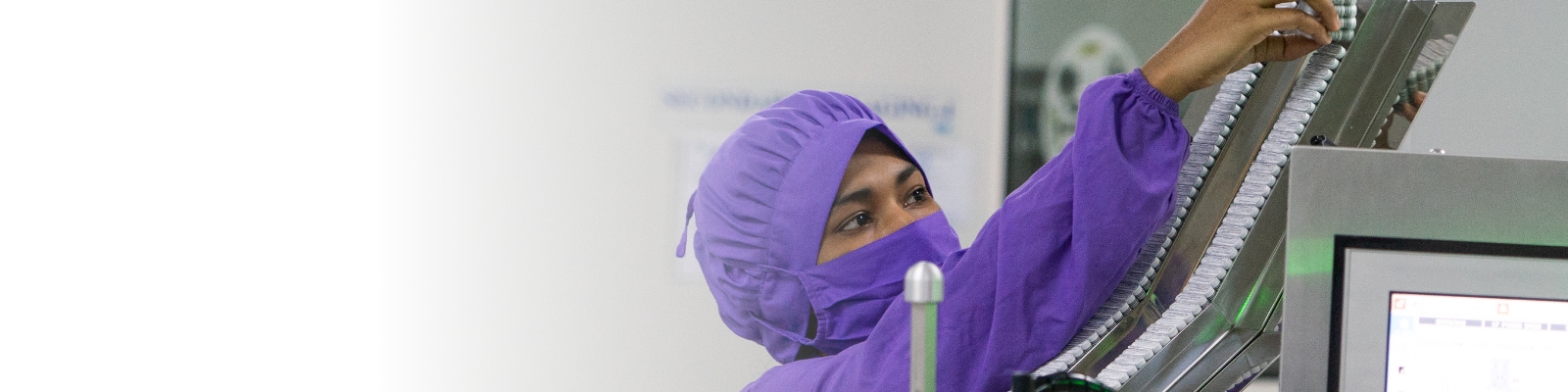 Worker in a purple gown, mask, and hairnet handling medicines in a manufacturing facility in Bangladesh