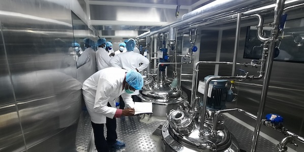 Laboratory staff in white gowns and blue hair nets checking equipment in Ghana