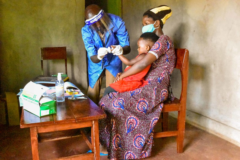 Community health worker administering rapid malaria test to mother and child.